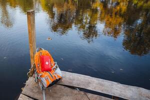 A serene autumn scene features a vibrant backpack resting by calm, reflective waters, creating a perfect setting for exploration and relaxation photo