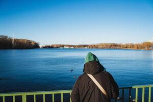 A person stands on a scenic bridge with an incredible view of a serene lake, enjoying the picturesque scenery and calming sounds of nature, experiencing profound tranquility photo