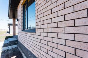 A close up view of a brick wall with a window embedded, creating an interesting architectural composition. The unique design adds character to the building, enhancing its aesthetic appeal photo