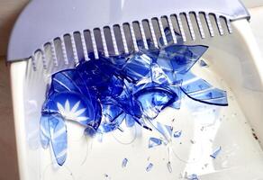 Group of broken blue cup glass with sharp fragment pieces isolated on horizontal white dustpan surface background. photo