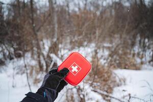 A person is standing in the snow, diligently holding a first aid kit firmly in their hand, prepared for any potential emergencies that might arise in such a wintery environment photo