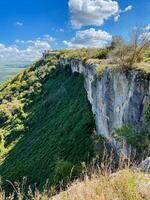 There is a towering cliff adorned with lush green trees, standing majestically against a backdrop of a clear blue sky that extends infinitely in all directions, inviting serenity and beauty photo