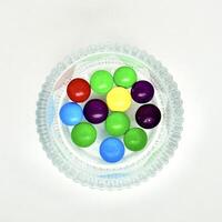 Group of colorful small round rainbow chocolate candy in round glass bowl isolated on square white background from top angle view. photo