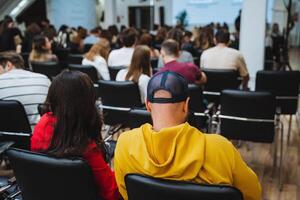 A man in a yellow hoodie is seated in front of a crowd at a community event photo