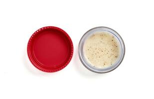 Opened lip scrub in small glass container with pink cap next to it isolated on horizontal white background. photo
