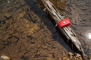 A red first aid kit is securely attached to a log floating in the water to provide emergency supplies in case of accidents or injuries. It features wood, water, and emergency preparedness photo
