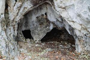 There exists a small cave nestled within the center of a rocky cliff, surrounded by towering stones and natural formations, creating a unique geological feature in the landscape photo
