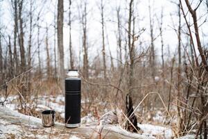 A thermos and a cup are sitting on a log in the woods photo