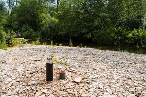 Near the tranquil river, a bottle and cup lay on the ground, blending seamlessly with the natural landscape. They are part of the peaceful environment, harmoniously coexisting with nature photo