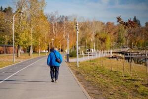 A man dressed in a blue jacket takes a leisurely stroll along a picturesque park path, fully enjoying the wonders of nature and wholeheartedly embracing the beautiful outdoors photo