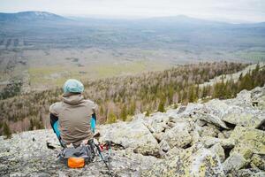 a man is sitting on top of a rocky mountain looking at the landscape photo