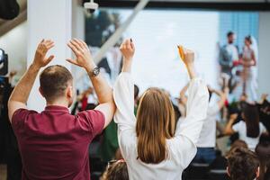 Crowd at an event making joint gesture in front of large display device photo