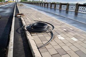A vibrant garden hose is casually sprawled across the sidewalk next to a bridge, crafting a lively scene that beautifully illustrates the intersection of nature and urban infrastructure photo