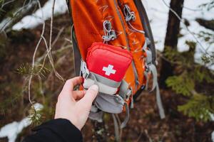 A red first aid kit with a white cross is in the pocket of the backpack, equipment for traveling alone, trekking in the mountains, bushcraft. photo