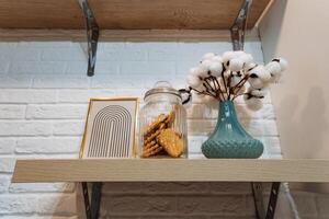 On a sturdy shelf, there sits a beautifully arranged vase filled with delicate cotton, alongside a charming jar full of delicious cookies, adding a cozy touch to any space photo