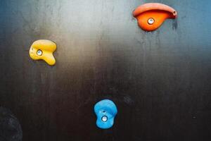 On a striking black wall, three unique climbing holds are suspended, showcasing their vibrant colors and distinct textures, creating an appealing visual element in the space photo