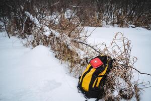 A vibrant yellow and black backpack is currently laying on the ground of the snowy landscape, contrasting beautifully with the white snow around it, creating a striking visual photo