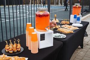 On the table, there is a drink dispenser filled with refreshing beverages, accompanied by an assortment of cups ready to be filled. Its perfect for any gathering or event photo