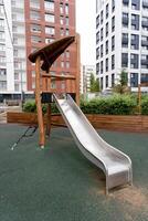 In a vibrant playground, there is a shiny stainless steel slide that stands out beautifully against the backdrop of tall buildings, creating a perfect scene for leisure and recreation photo