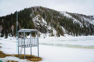 Snowcovered lifeguard tower on shore of freezing lake in mountainous landscape photo