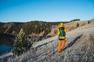 Hiking with a backpack in the mountains, tourist route, a man walking on frozen ground against the background of the forest, trekking on the hills, rear view of a hiker. photo