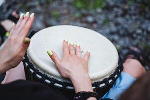 A talented musician, with a passion for percussion instruments, skillfully plays the djembe drum with green manicured nails, displaying her musical talent and love for music photo