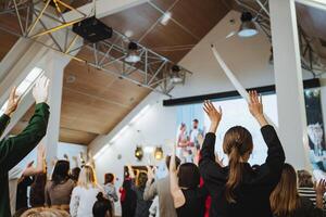 A crowd enjoying an art event, raising hands in a room with a high ceiling photo