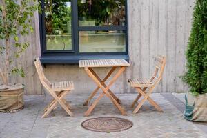 A charming rustic wooden table, accompanied by matching chairs, is set up on a cozy and inviting patio that sits in front of a large window, allowing ample natural light to flood the space photo