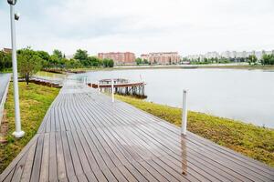 A serene park features a wooden pathway leading to a calm lake, integrating natural beauty with manmade elements. The scene highlights the harmony between nature and human design photo