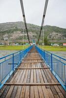 A suspension bridge stretches over a river in a tranquil village surrounded by mountains, offering a captivating view and creating a serene environment for visitors to appreciate photo