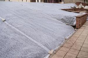On top of a structure, a roof is covered with a gray tarp that provides protection and coverage from various weather elements, helping to shield the underlying materials photo