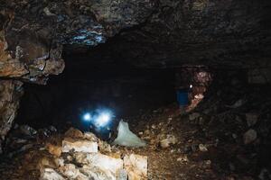 A man stands alone in a dark, eerie cave, firmly holding a powerful flashlight that unveils the breathtaking rock formations and casts intricate, mesmerizing shadows all around him photo