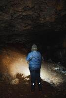 A solitary figure stands quietly in a dimly lit cave, holding a flashlight that casts light on the rocky walls and surrounding shadows, creating an intriguing and captivating air of mystery photo