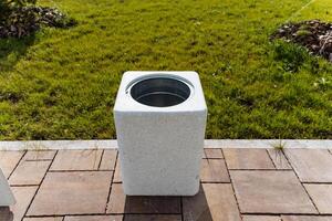 In front of a grassy field, there is a white trash can placed on a brick patio, creating a contrast between the patios composition and the natural greenery surrounding it photo