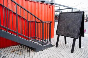 In front of a striking red staircase, there is a prominent black sign positioned right beside it, drawing attention to both the structure and its accompanying information photo