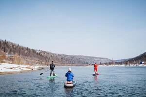 A group of people floats down the river on paddleboards, a man stands on a board with a paddle, paddling on a sunny day on a lake. photo