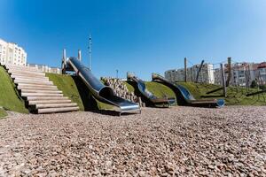A playground in urban setting with slides and staircases amid cityscape on sloping asphalt ground, perfect for leisure activities. It blends into the landscape seamlessly photo
