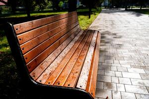 In a lovely park, there is a sturdy wooden bench that is comfortably sitting on a wellmaintained brick sidewalk, inviting visitors to sit and enjoy the natural surroundings photo
