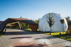 In the center of the expansive park, there is an impressive large white dome tent that stands out remarkably among its surroundings, attracting attention with its unique shape and color photo