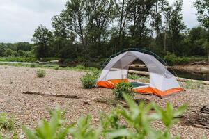 A camping tent by a serene river in a quiet forest provides a peaceful setting for outdoor activities, surrounded by lush greenery, perfect for relaxation and tranquility photo