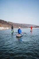 SUP boarders sailing on a mountain river, rear view of people standing on a board with a paddle, a team of athletes, outdoor activities on the water. photo