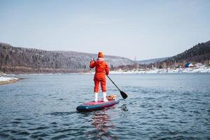 A woman stands on a SUP board and paddles, a man in a red protective suit floats on a board with a paddle on a mountain river, rear view. photo