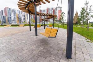 A wooden swing is beautifully hanging from a tall pole in a park photo