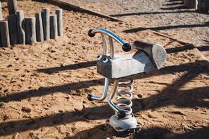 A beautifully crafted rocking horse can be seen sitting in the soft sand at a colorful playground, inviting children to come and play with it. Its a charming sight for all photo