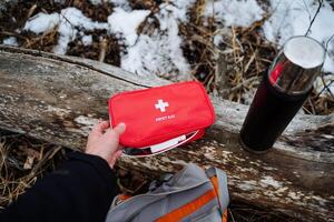 An essential first aid kit is placed on a rustic log surrounded by a picturesque winter landscape, evoking feelings of warmth and preparedness for any unexpected situation photo