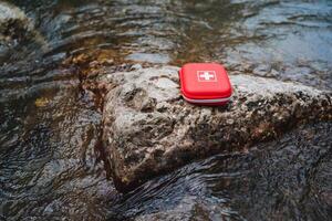 A red first aid kit placed on a rock in a flowing stream, symbolizing emergency preparedness, outdoor safety, and the importance of health and safety in natural environments photo