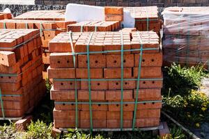 A pallet of neatly stacked red clay bricks wrapped in plastic is ready for use on a sunny day at a construction site, providing building materials for construction work photo
