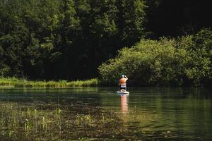 Amidst the tranquility of nature, a man peacefully paddle boards on a serene lake, finding solace in the reflections of trees and the beauty of the countryside photo