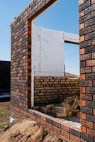 Focused on construction progress of a brick house with exposed structure and masonry work at building site, showcasing stages of building a residential property photo