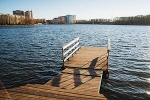 A beautifully designed wooden dock reaches out into the serene and calm waters of the lake, creating a striking contrast with the lively, vibrant cityscape that lies in the background photo